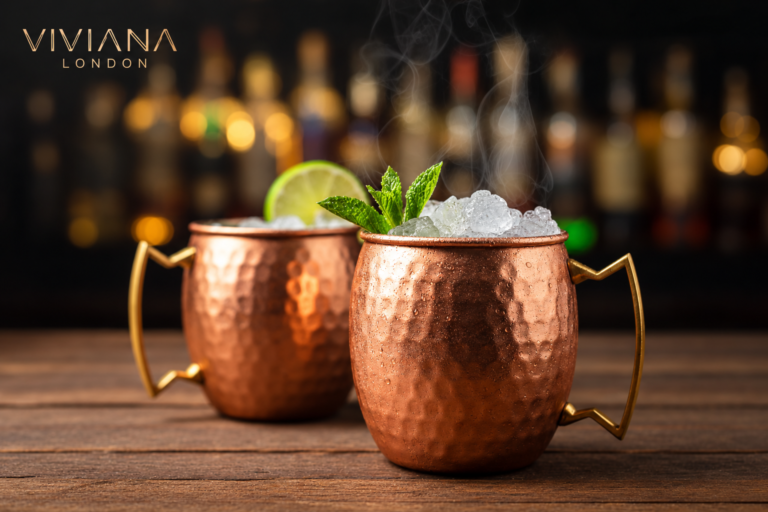 A hand-hammered pure copper Moscow Mule mug filled with an iced cocktail and fresh mint garnish on a dark bar surface.