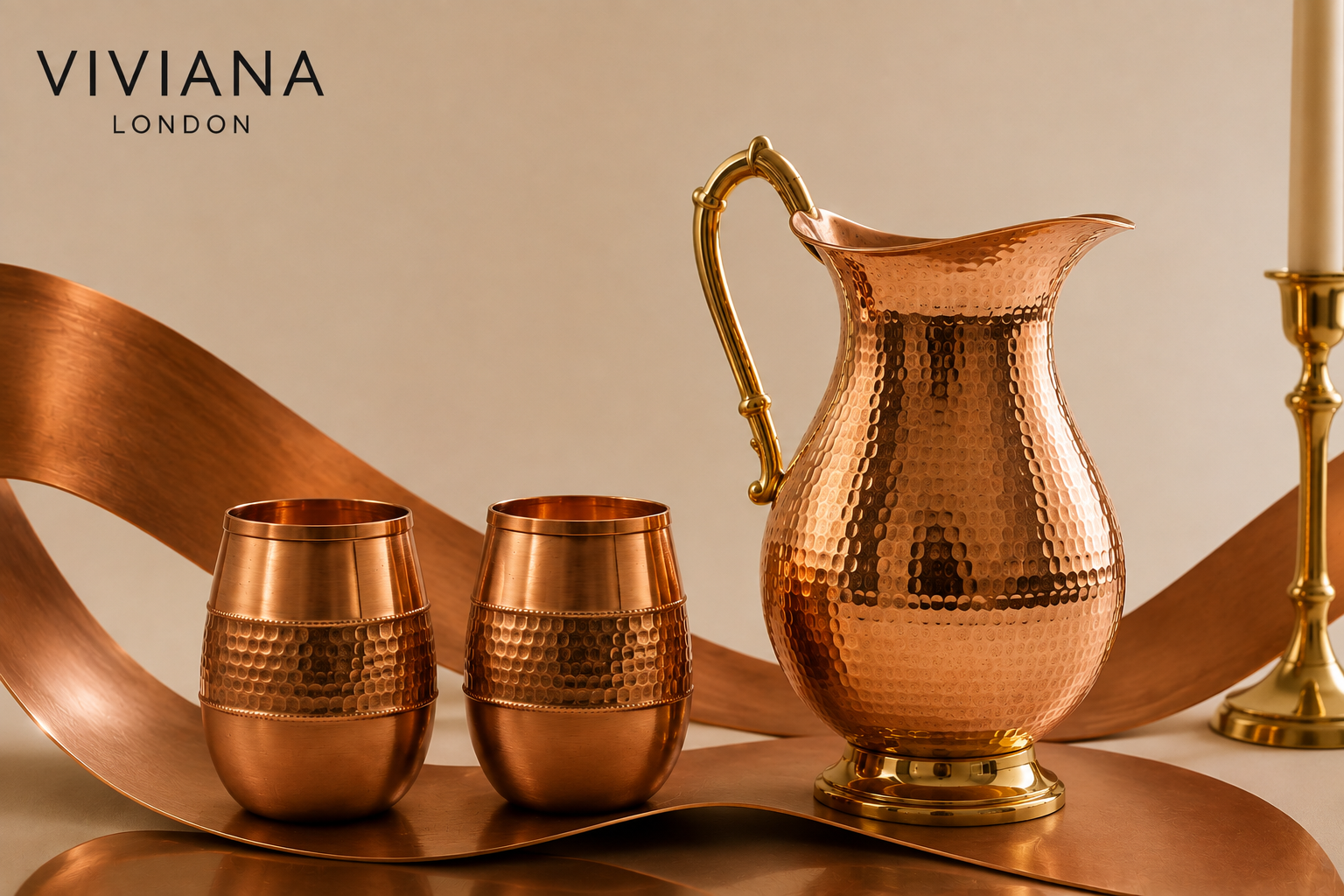 Hand-hammered pure copper bottle and jug set styled on a kitchen wooden counter next to a glass of water