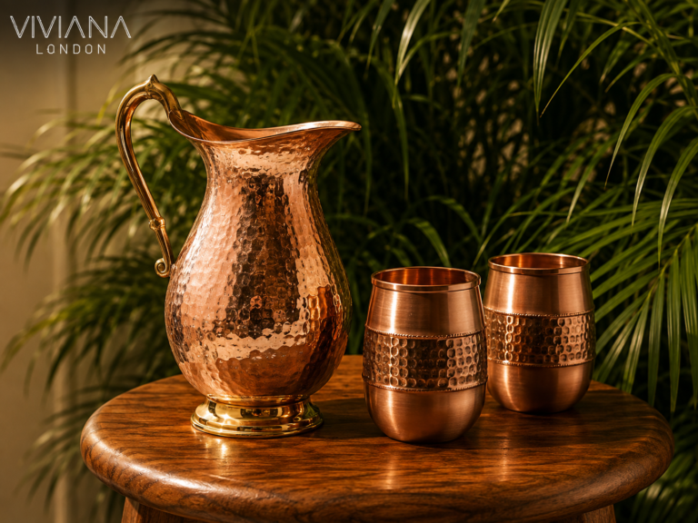 Hand-hammered solid copper water bottle and jug styled on a clean wooden table next to a glass of water